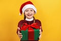 Happy child with christmas present. Little girl in santa claus hat gives a gift on a yellow background Royalty Free Stock Photo