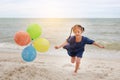 Happy child with colorful balloons running on the beach