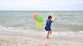 Happy child with colorful balloons running on the beach