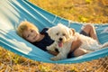 Happy child, cute boy, swinging on hammock swing in garden with his pet dog