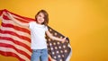 Happy child, cute girl with American flag on yellow studio background. USA celebrate July 4th, independence Day.