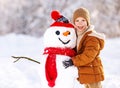 Happy child cute little boy in warm clothes with snowman in snowy winter park Royalty Free Stock Photo