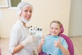 Happy child in dentist chair with female doctor showing thumbs up at dental clinic.