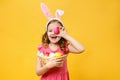 Happy child in the ears of a bunny holds an Easter egg and a basket. Portrait of a little girl on a yellow background Royalty Free Stock Photo