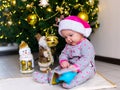 Happy child finding a gift under the tree. A girl in a pink Santa hat