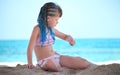 Happy child girl in bikini swimsuit playing with sand on seaside beach during summer tropical vacation Royalty Free Stock Photo