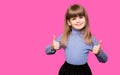 Happy child girl in sweater showing thumbs up and looking at camera isolated over pink background