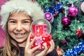 Happy child girl in a Christmas hat holding glass globe gift of