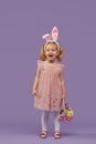 Happy child girl in costume Easter bunny rabbit with ears and a basket with eggs. Little girl on a purple Royalty Free Stock Photo