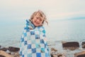 Happy child girl covered in quilt blanket, cozy summer holidays on seaside