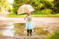 Happy child girl with an umbrella and rubber boots in puddle on summer walk Royalty Free Stock Photo