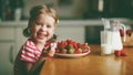 happy child girl drinks milk and eats strawberries in summer home kitchen Royalty Free Stock Photo