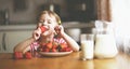 Happy child girl drinks milk and eats strawberries in summer home kitchen Royalty Free Stock Photo