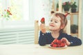 Happy child girl eats strawberries in summer home kitchen Royalty Free Stock Photo