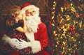 Happy child girl embraces Santa Claus, and tells him secret