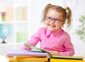 Happy child girl in glasses reading books in room