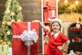 Happy child girl holding a big red gift box. Kid having fun near Christmas tree indoors. Winter delivery service for Royalty Free Stock Photo