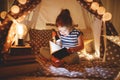 Happy child girl laughing and reading book in dark in tent at ho Royalty Free Stock Photo