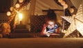 Happy child girl laughing and reading book in dark in tent at ho Royalty Free Stock Photo