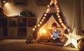 Happy child girl laughing and reading book in dark in tent at ho Royalty Free Stock Photo
