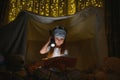 Happy child girl laughing and reading book in dark in a tent at home Royalty Free Stock Photo