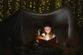 Happy child girl laughing and reading book in dark in a tent at home Royalty Free Stock Photo