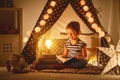 Happy child girl laughing and reading book in dark in tent at ho Royalty Free Stock Photo