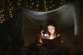 happy child girl laughing and reading book in dark in a tent at home. Royalty Free Stock Photo