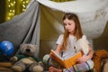 happy child girl laughing and reading book in dark in a tent at home. Royalty Free Stock Photo