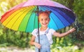 Happy child girl laughs and plays under summer rain with an umbrella. Royalty Free Stock Photo