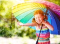 Happy child girl laughs and plays under summer rain with an umbrella. Royalty Free Stock Photo