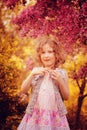 Happy child girl in pink dress playing outdoor in spring garden near blooming crabapple tree Royalty Free Stock Photo