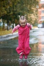 Happy child girl with pink rubber pants and boots in puddle on an autumn walk, seasonal fun childhood game