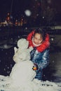 Happy child girl plaing with a snowman on a snowy winter walk.A teenage girl sculpts a snowman Royalty Free Stock Photo