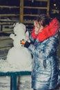 Happy child girl plaing with a snowman on a snowy winter walk.A teenage girl sculpts a snowman