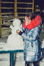 Happy child girl plaing with a snowman on a snowy winter walk.A teenage girl sculpts a snowman