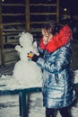 Happy child girl plaing with a snowman on a snowy winter walk.A teenage girl sculpts a snowman Royalty Free Stock Photo
