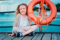 Happy child girl plays with rescue ring on wooden pier with sea background Royalty Free Stock Photo