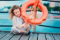 Happy child girl plays with rescue ring on wooden pier with sea background Royalty Free Stock Photo