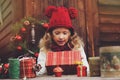 Happy child girl in red hat and scarf wrapping Christmas gifts at cozy country house, decorated for New Year and Christmas Royalty Free Stock Photo