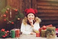 Happy child girl in red hat and scarf wrapping Christmas gifts at cozy country house, decorated for New Year and Christmas Royalty Free Stock Photo