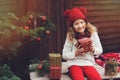 Happy child girl in red hat and scarf wrapping Christmas gifts at cozy country house, decorated for New Year and Christmas Royalty Free Stock Photo