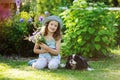 happy child girl relaxing in summer garden with her spaniel dog, wearing gardener hat and holding bouquet of flowers Royalty Free Stock Photo