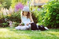 Happy child girl relaxing in summer garden with her spaniel dog, wearing gardener hat and holding bouquet of flowers Royalty Free Stock Photo