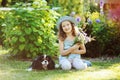 Happy child girl relaxing in summer garden with her spaniel dog, wearing gardener hat and holding bouquet of flowers. Royalty Free Stock Photo