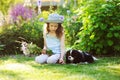 happy child girl relaxing in summer garden with her spaniel dog, wearing gardener hat and holding bouquet of flowers Royalty Free Stock Photo