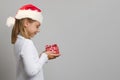 Happy child girl in Santa hat looking at red present box on white studio wall background with copy space Royalty Free Stock Photo