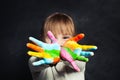 Happy child girl showing her colorful painting hands on classroom blackboard background portrait