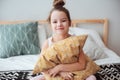 happy child girl sitting on bed and hugs pillow, waking up in early morning or going to sleep Royalty Free Stock Photo