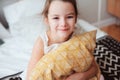 Happy child girl sitting on bed and hugs pillow, waking up in early morning or going to sleep Royalty Free Stock Photo